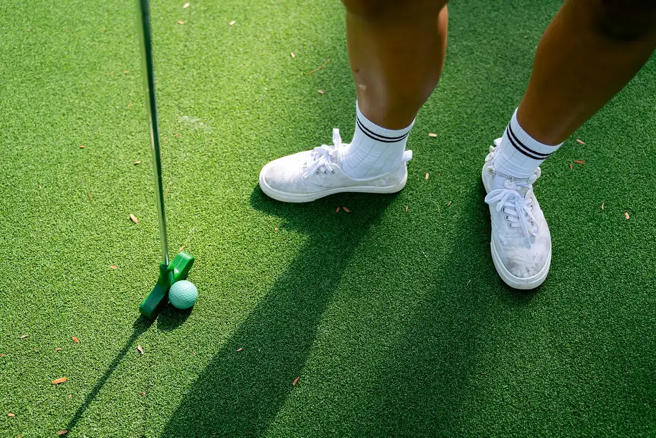 Närbild på en person som puttar med en minigolfklubba på konstgräs