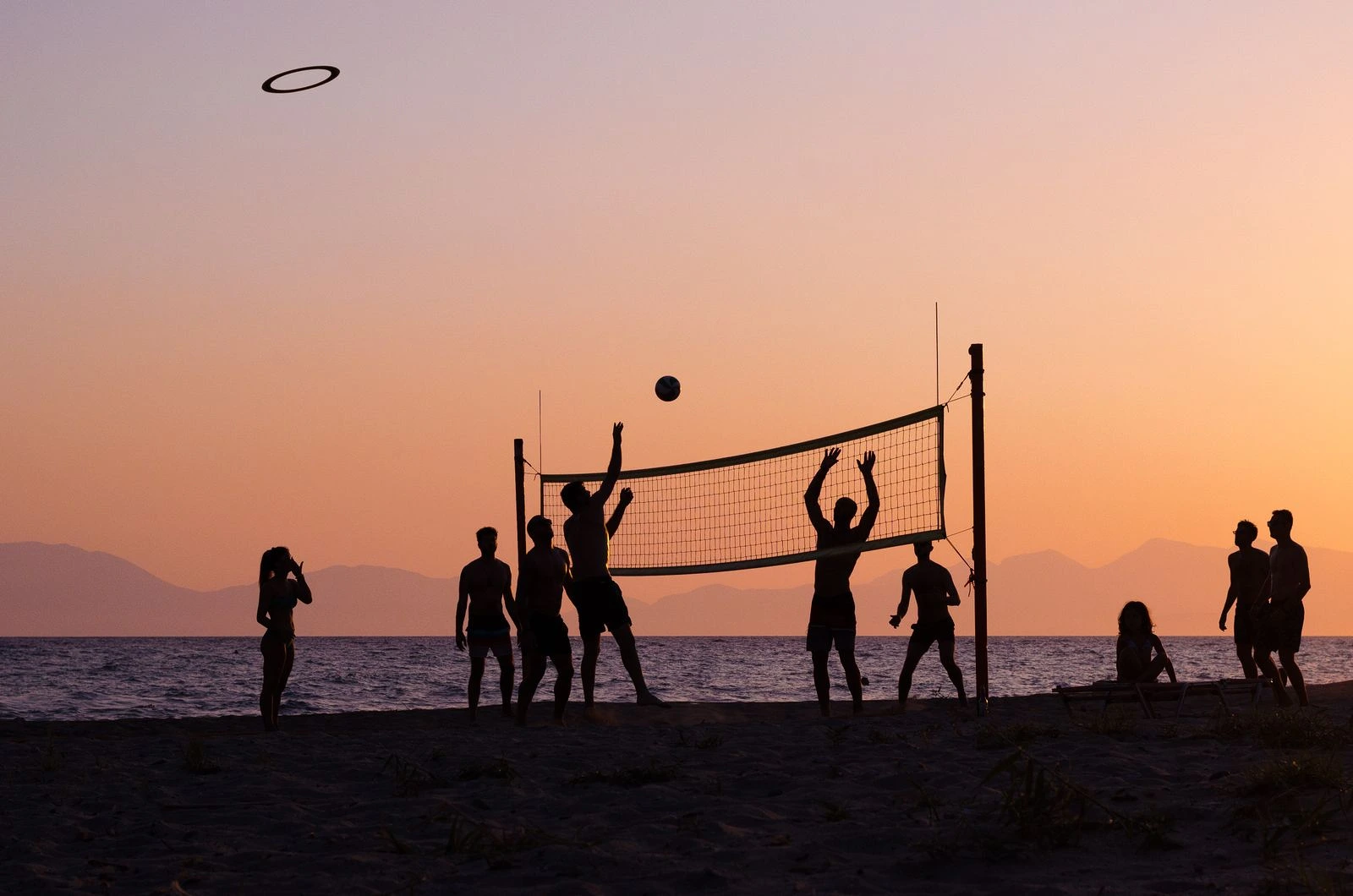 Människor som spelar beachvolleyboll på sand i varmt kvällsljus